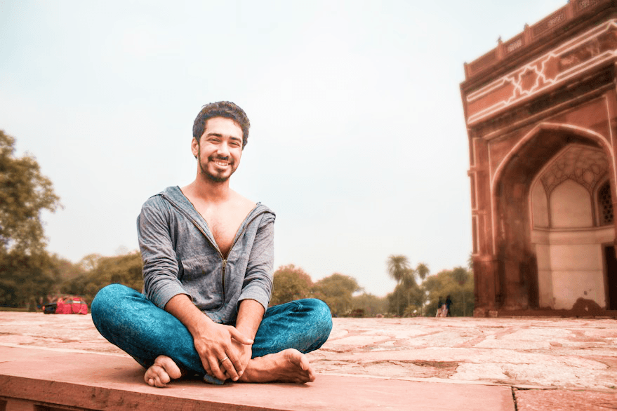 A teacher sitting cross-legged outdoors near a historic archway