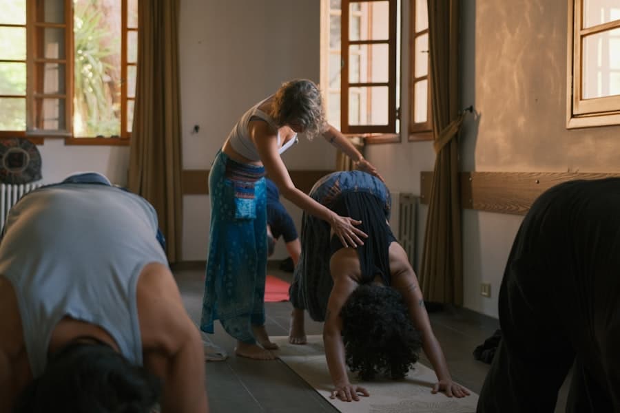A yoga teacher gently adjusting a student in a downward-facing dog pose